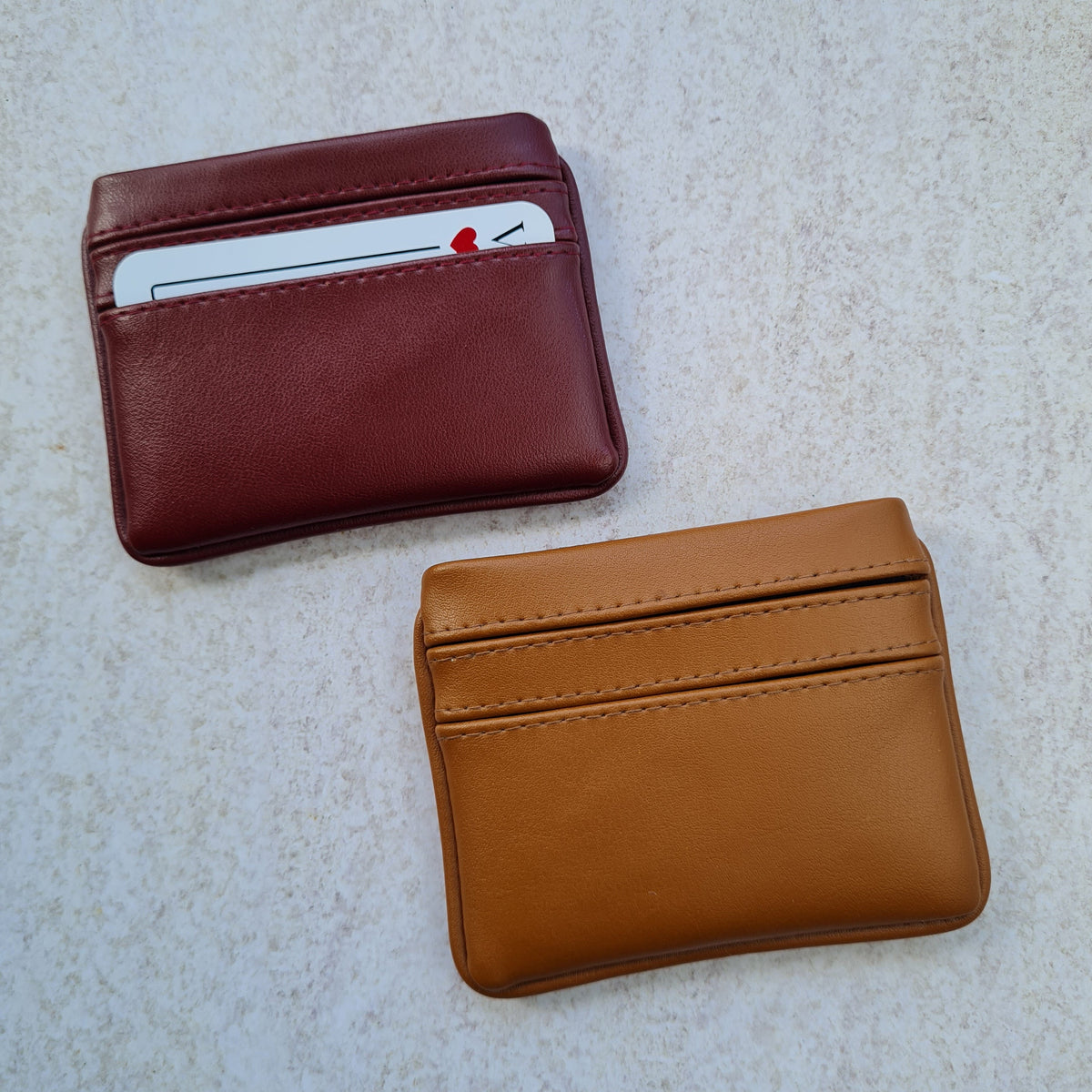 Two card wallets in cherry red and caramel tan with 5 card pockets made from vegan cactus leather with subtle piping detail on edge