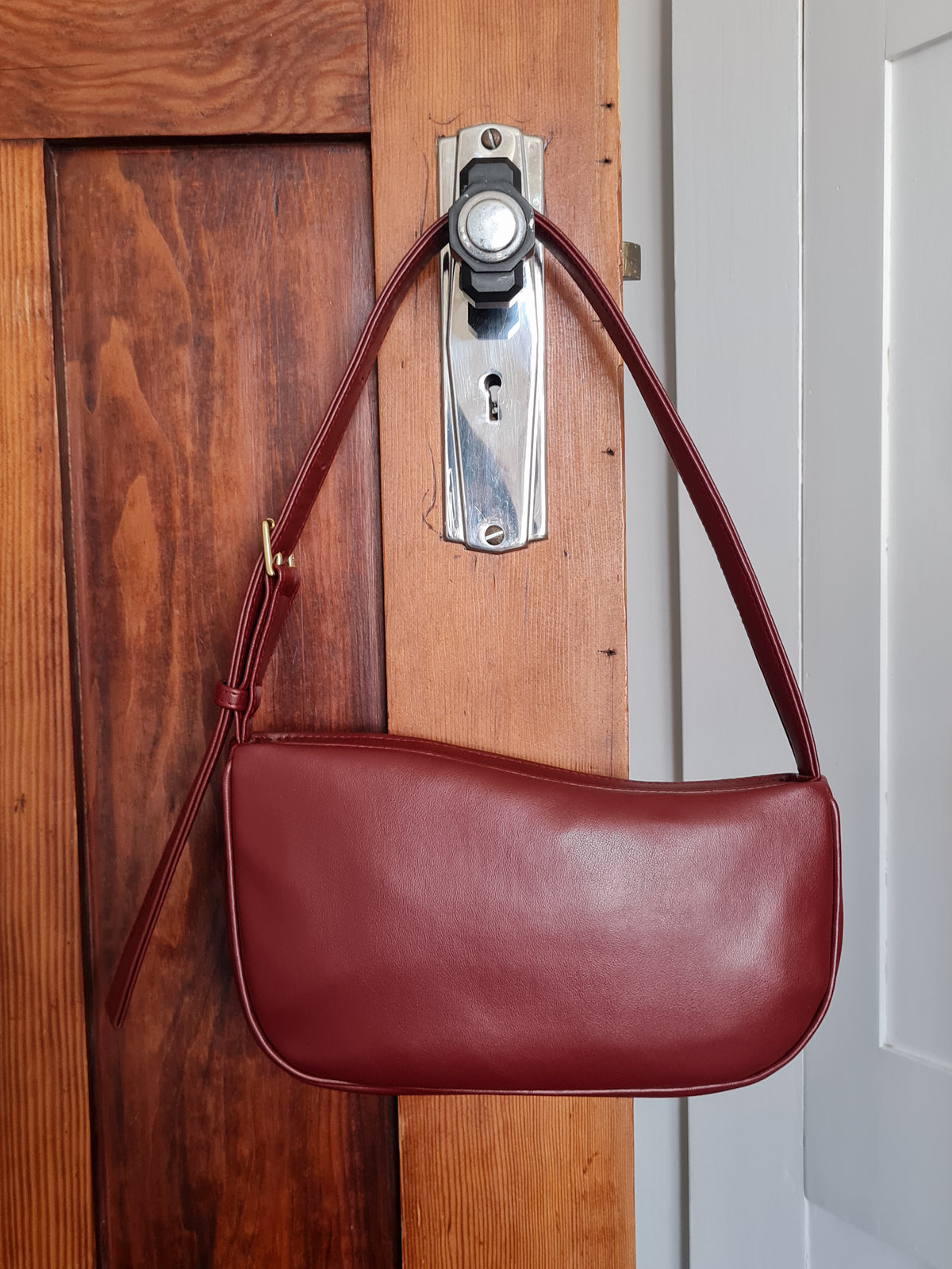 A dark red cactus leather shoulder bag with a curved top edge, crescent-shaped body and a single shoulder strap with a buckle