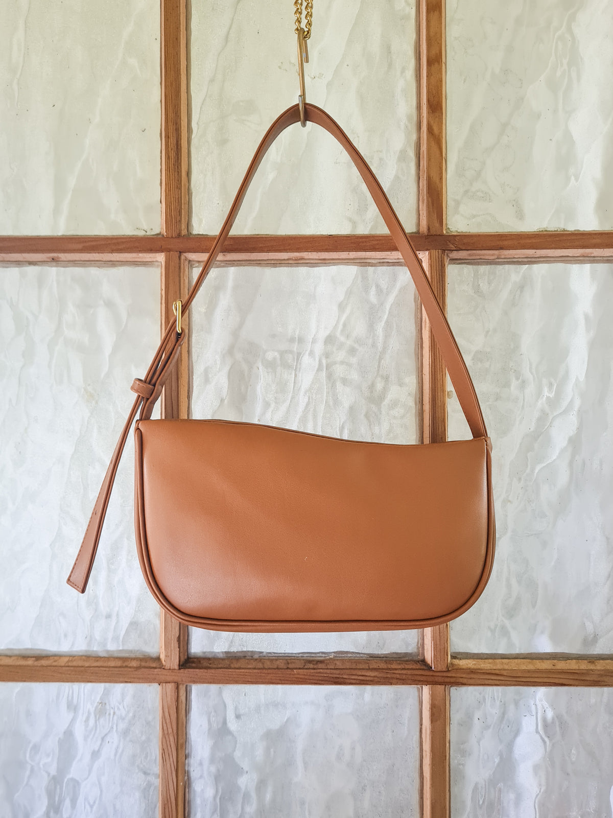 A tan cactus leather shoulder bag with a curved top edge, crescent-shaped body and a single shoulder strap with a buckle