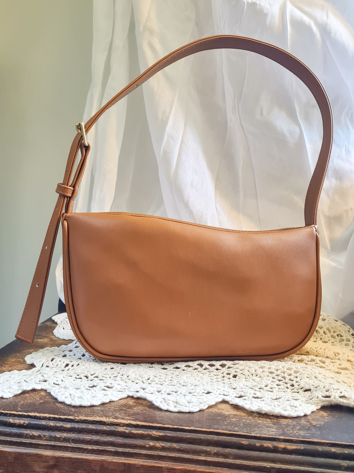 A tan cactus leather shoulder bag with a curved top edge, crescent-shaped body and a single shoulder strap with a buckle