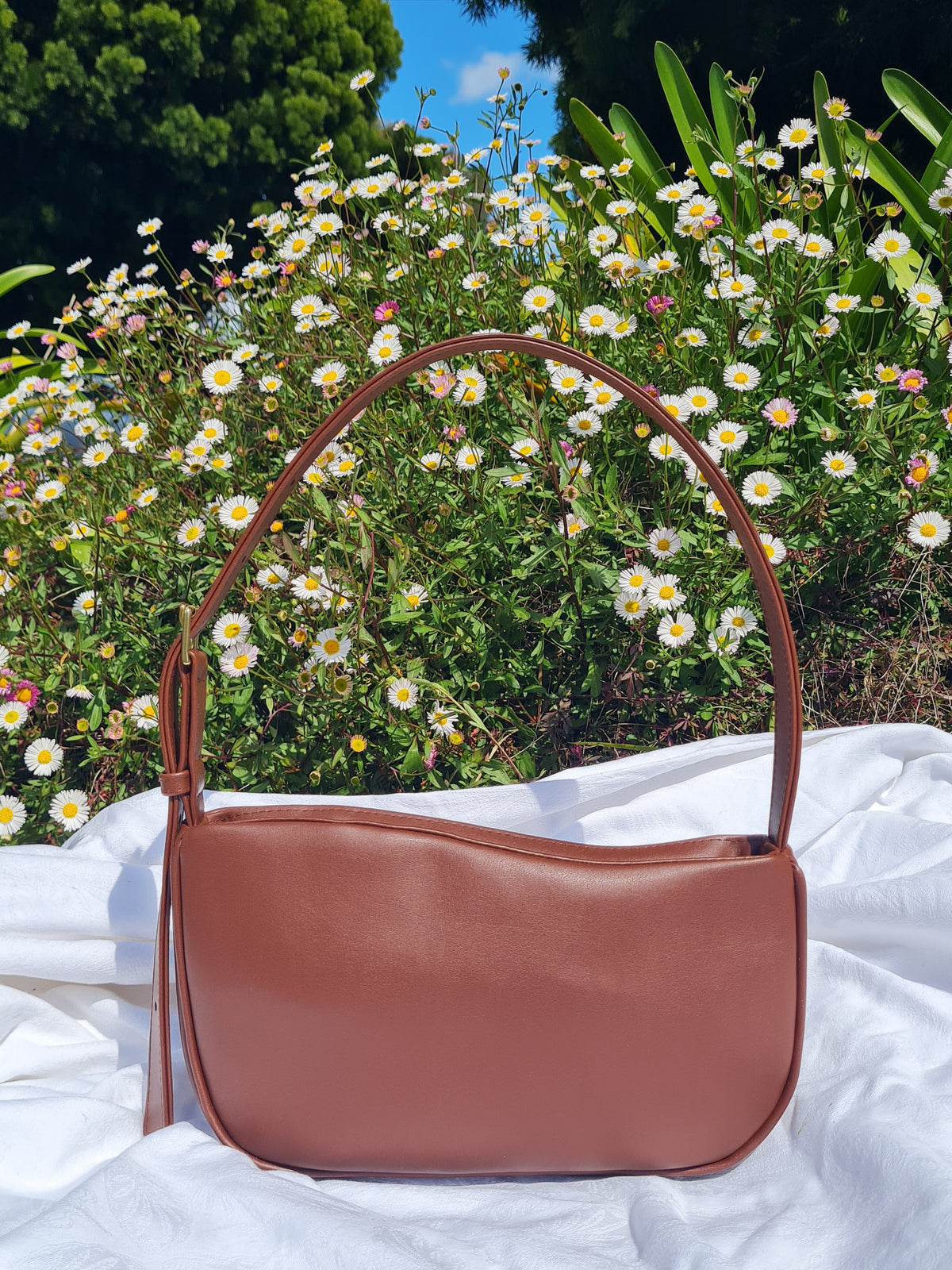 A chocolate brown cactus leather shoulder bag with a curved top edge, crescent-shaped body and a single shoulder strap with a buckle